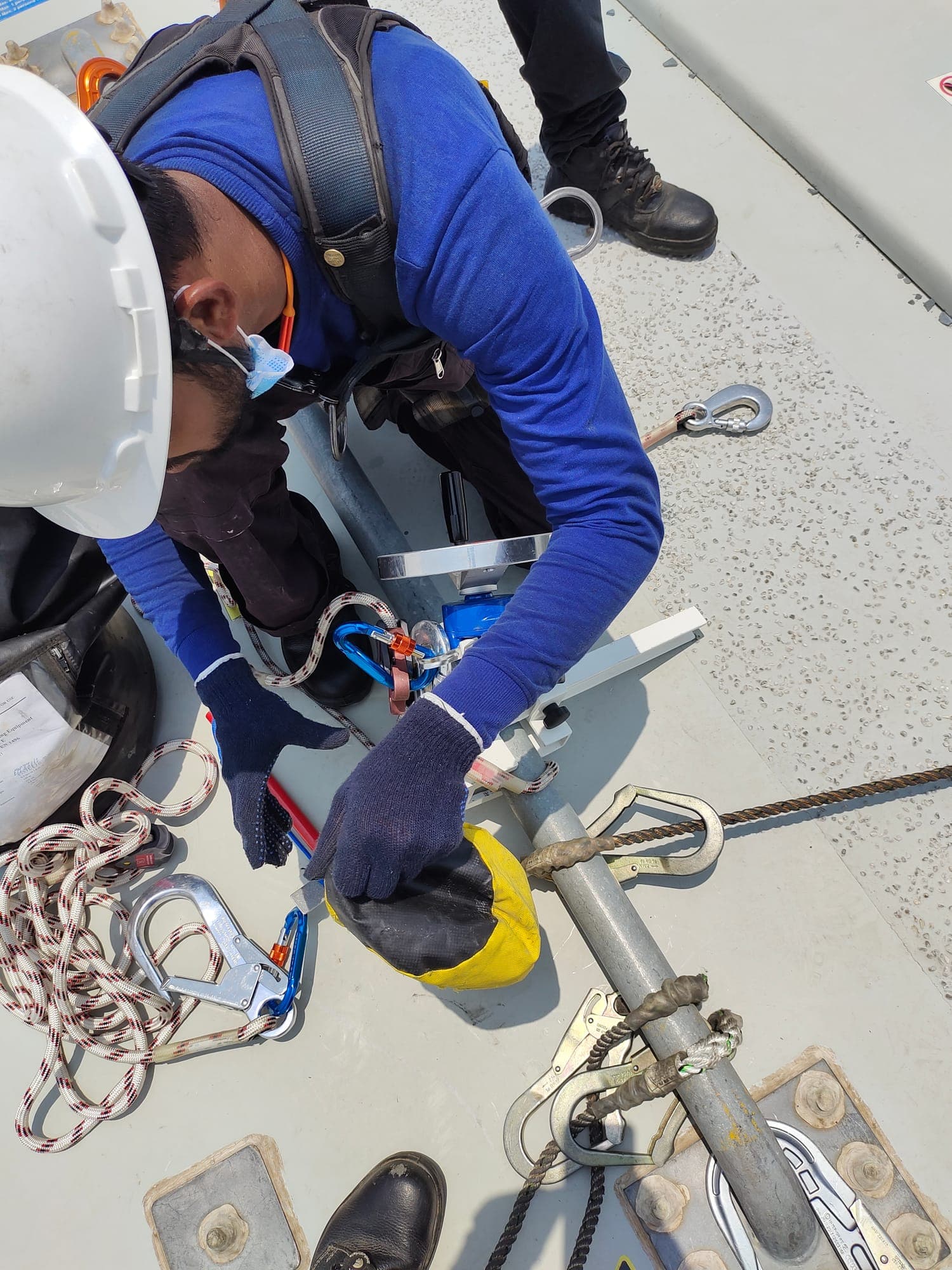 Gloved hands attaching a rescue descender to rigging hardware during advanced rescue training on a nacelle roof