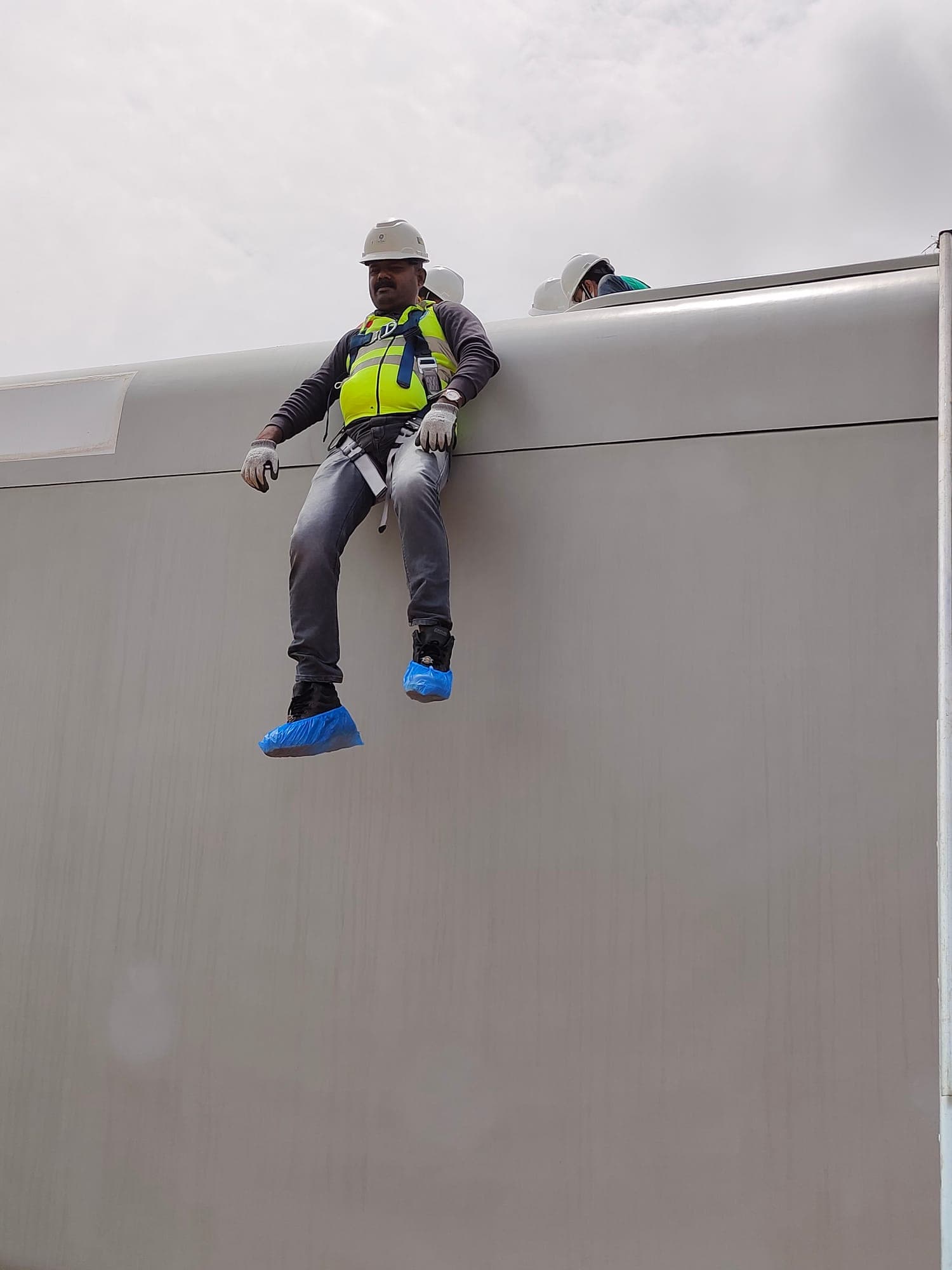 Technician in a harness descending on a rope over the edge of a wind turbine nacelle during rescue training