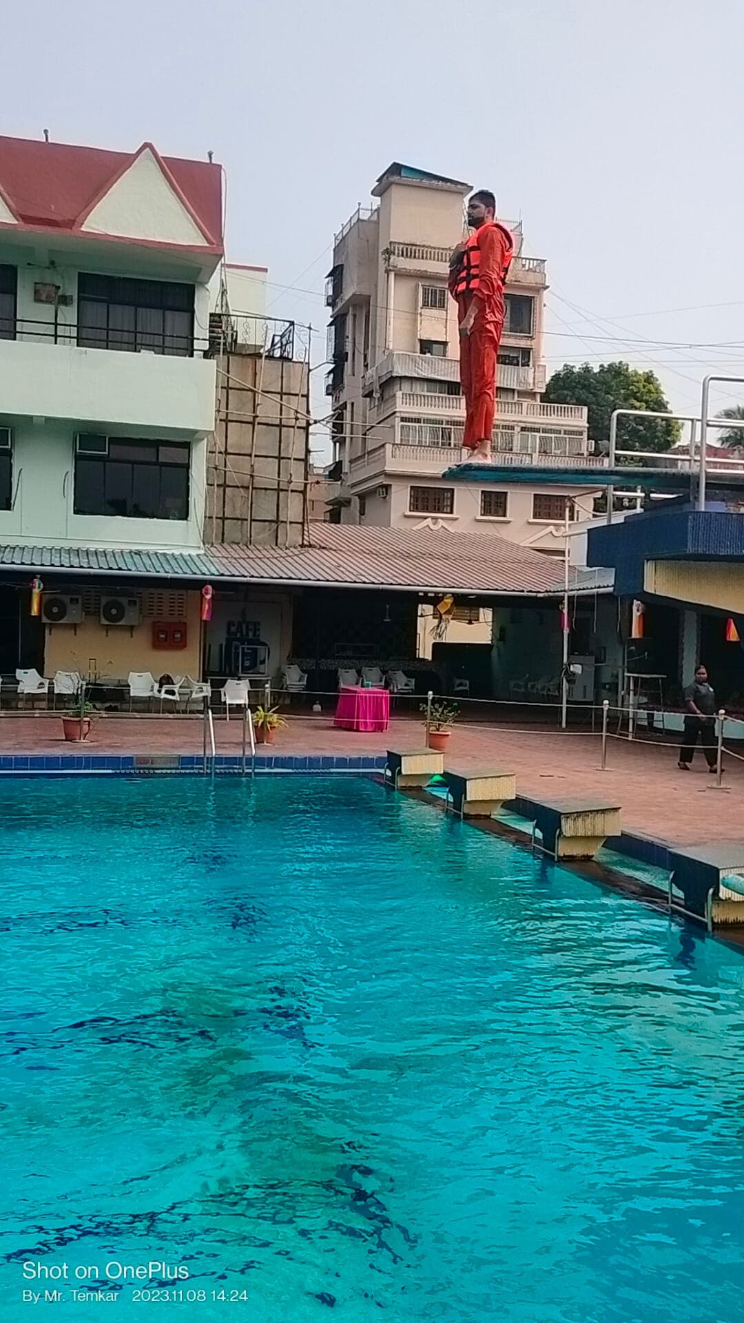 Participant in an immersion suit and lifejacket standing on a raised platform above a training pool, preparing to enter the water during sea survival training