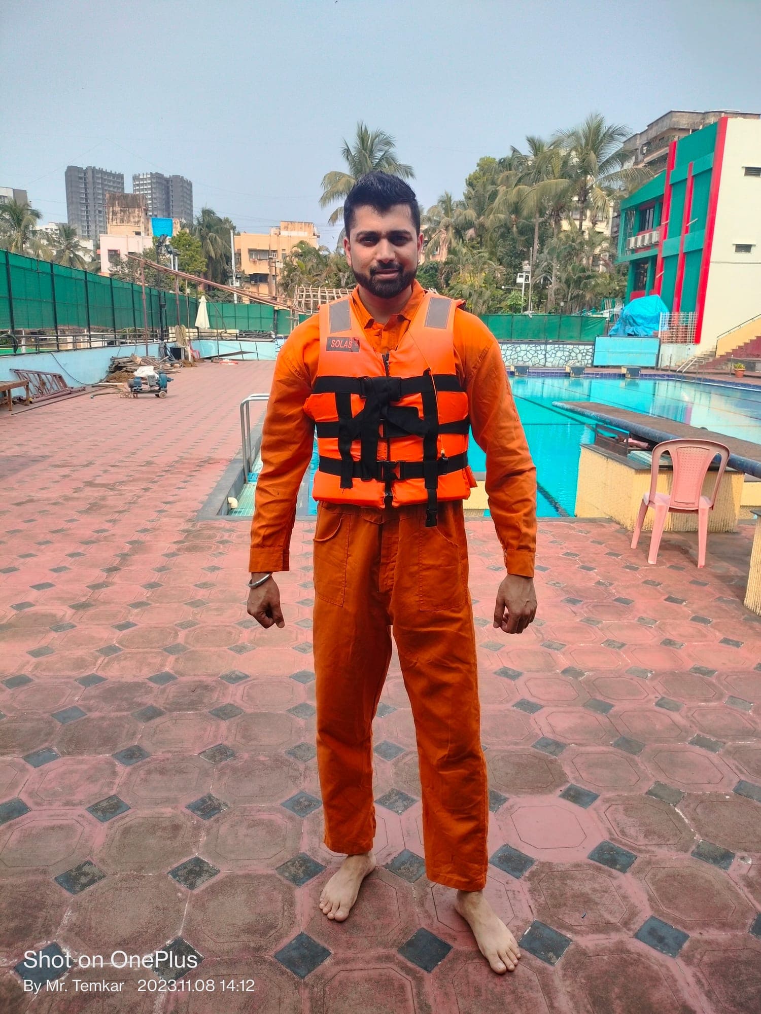 Participant wearing an orange immersion suit and a SOLAS-marked lifejacket at the side of a training pool during sea survival training