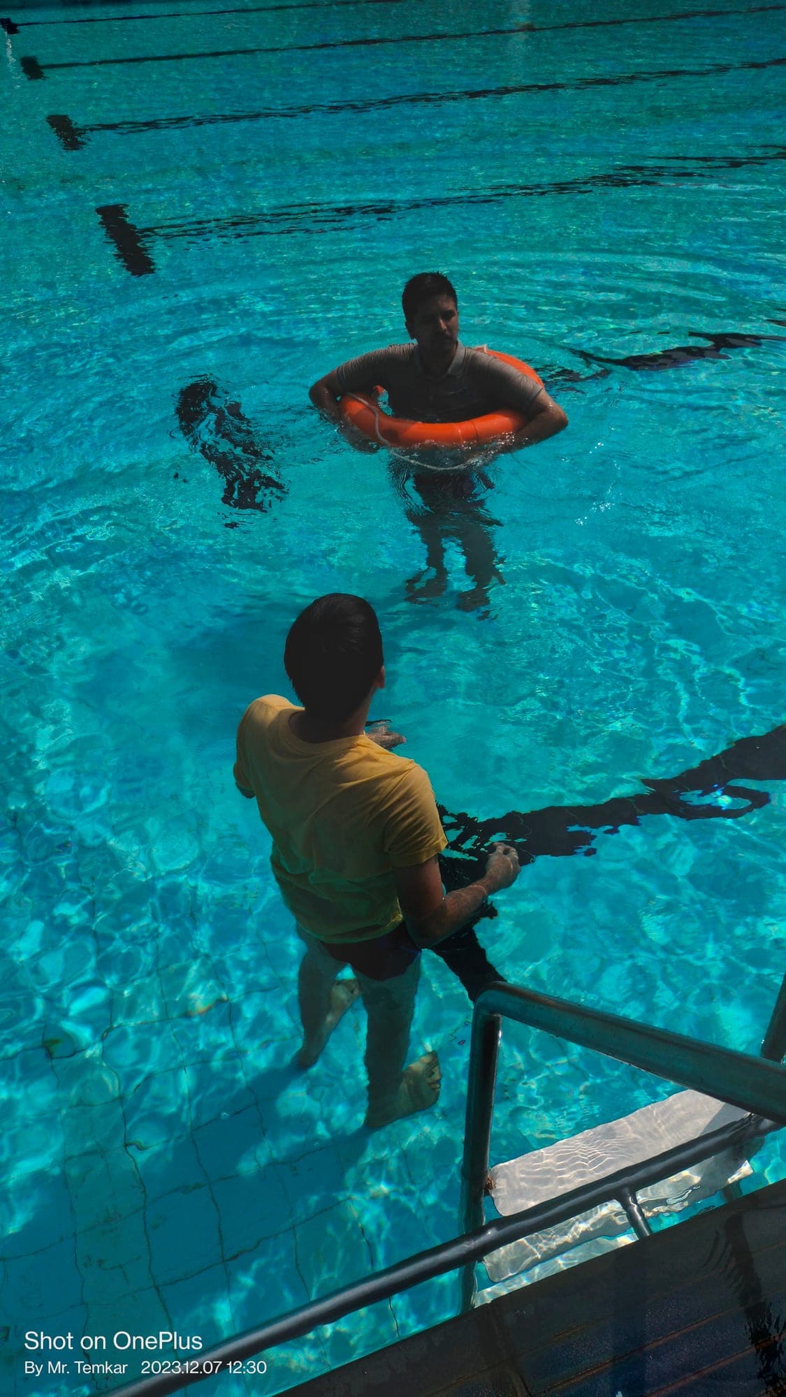 Participant in the water inside a lifebuoy ring while another participant assists from the poolside during sea survival training
