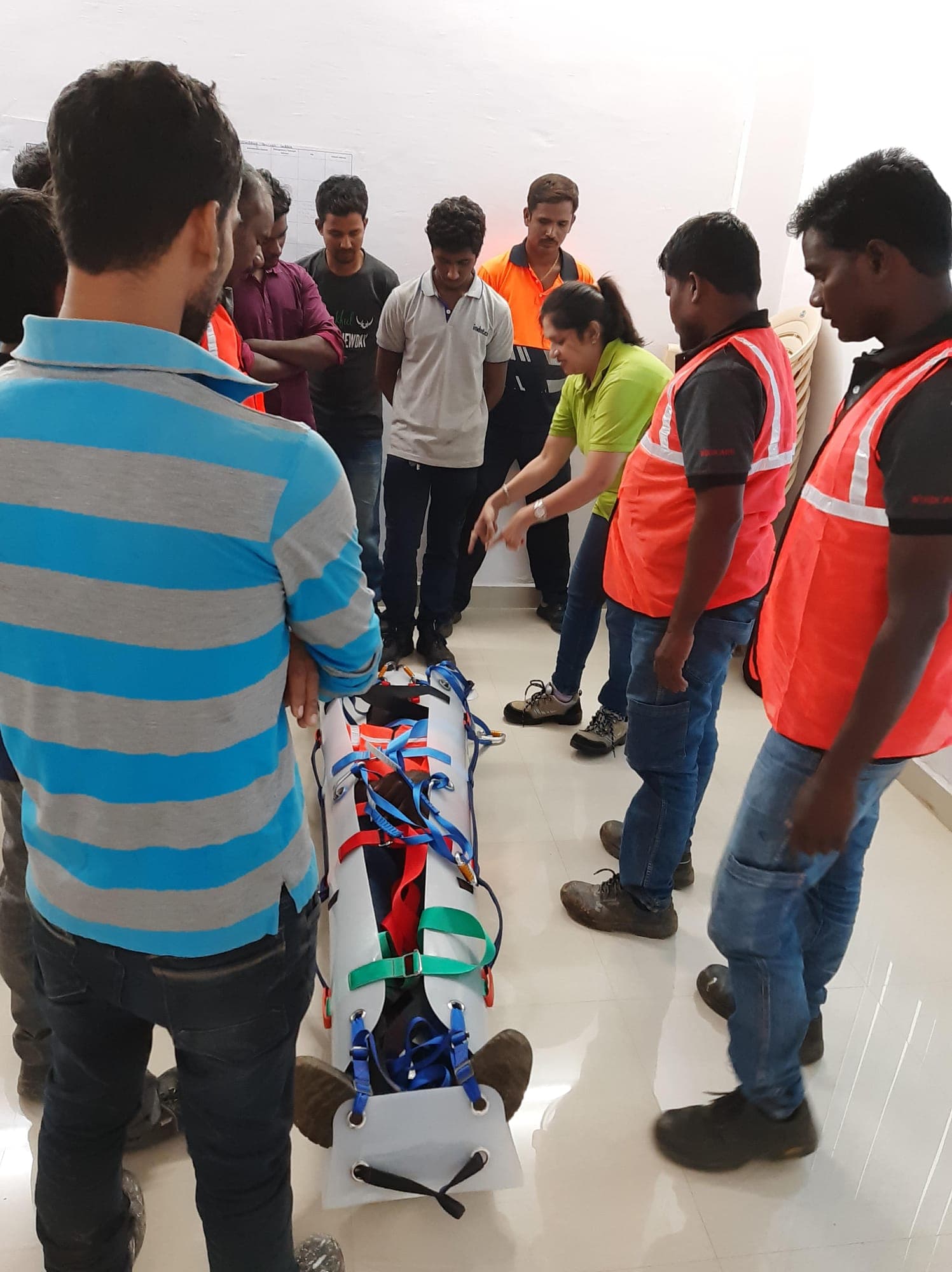 Workers in helmets and high-visibility vests immobilising a volunteer casualty on a spine board at a site