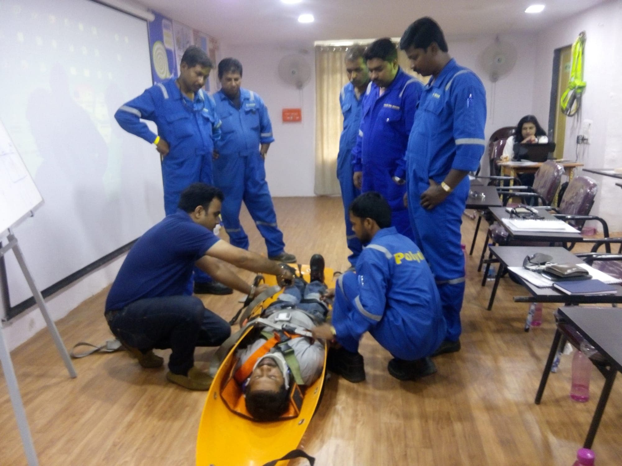 Team securing a simulated casualty into a basket stretcher with straps while others observe