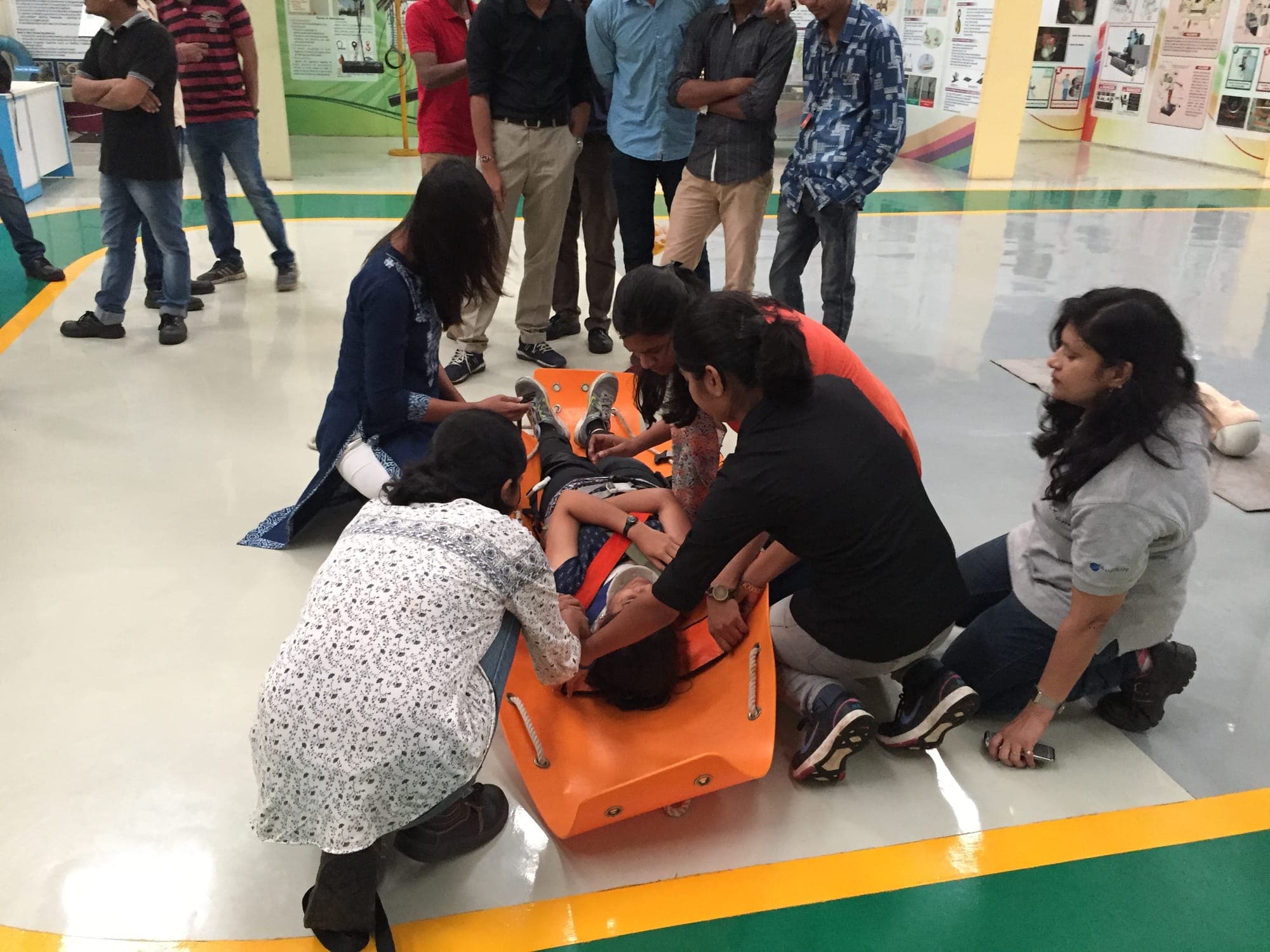 Participants strapping a volunteer casualty onto a rescue stretcher on a factory floor