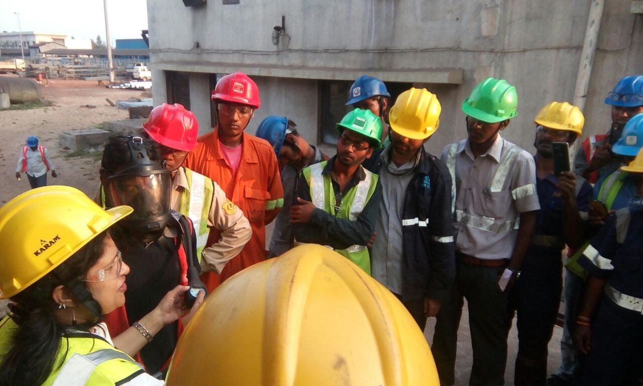 Trainer holding a helmet while briefing site workers in helmets and high-visibility vests