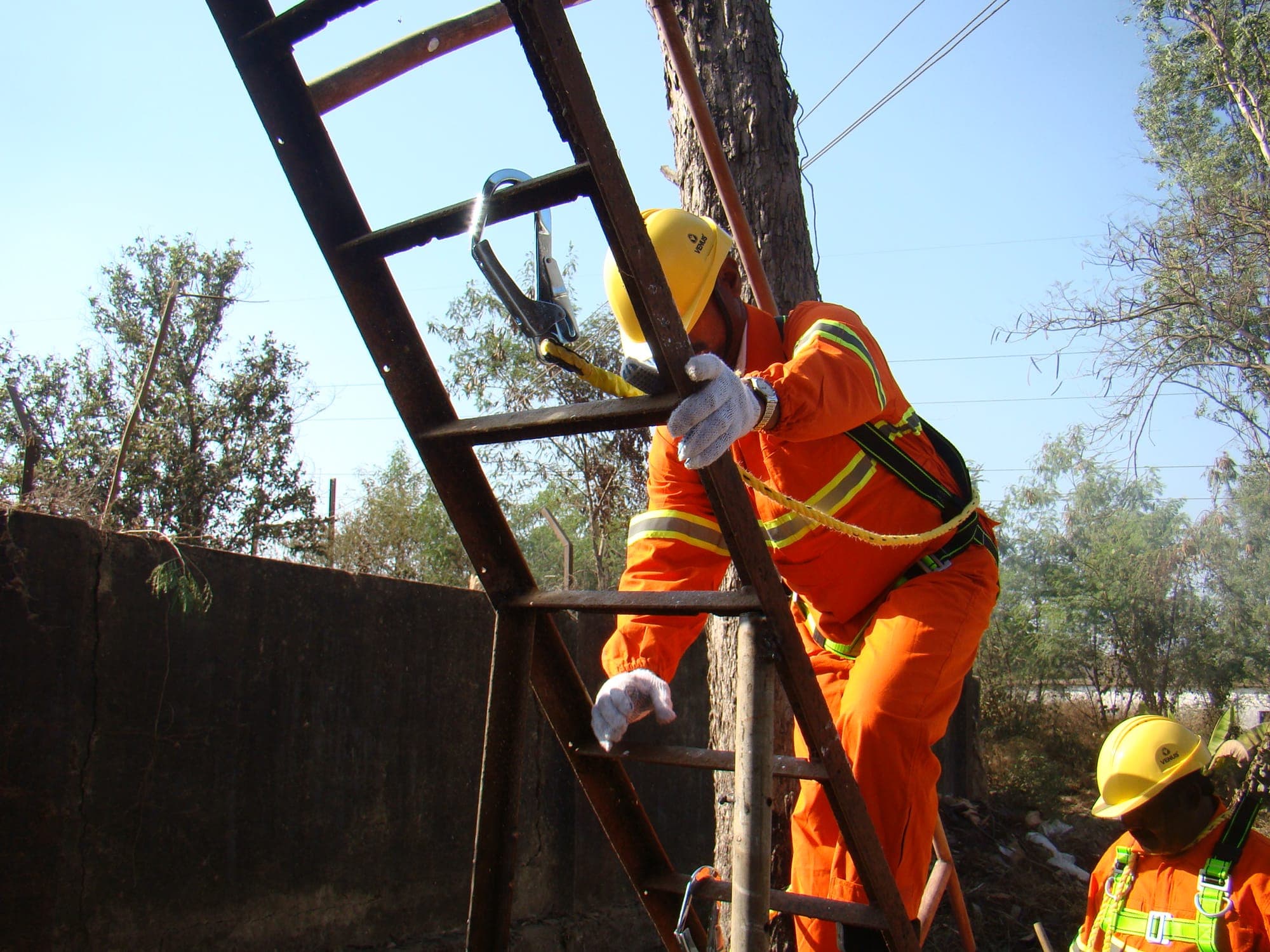 Trainee in coveralls and harness climbing a fixed vertical ladder during a practical exercise