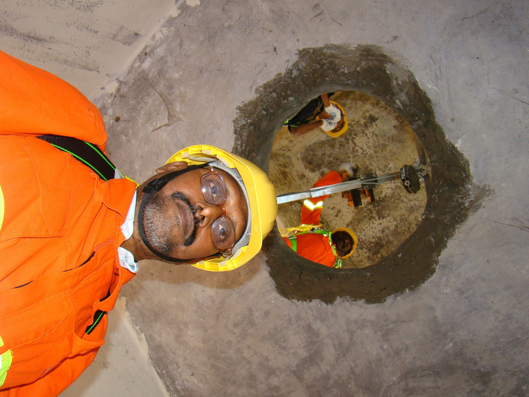Trainee in a hard hat emerging from a circular confined space opening at ground level