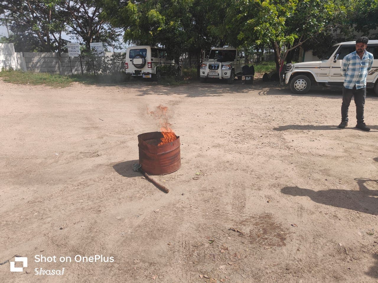 Trainer supervising a drum fire during an extinguisher demonstration in an open yard