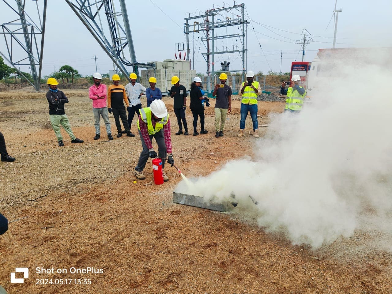 Participants practising with fire extinguishers on open ground with a group watching