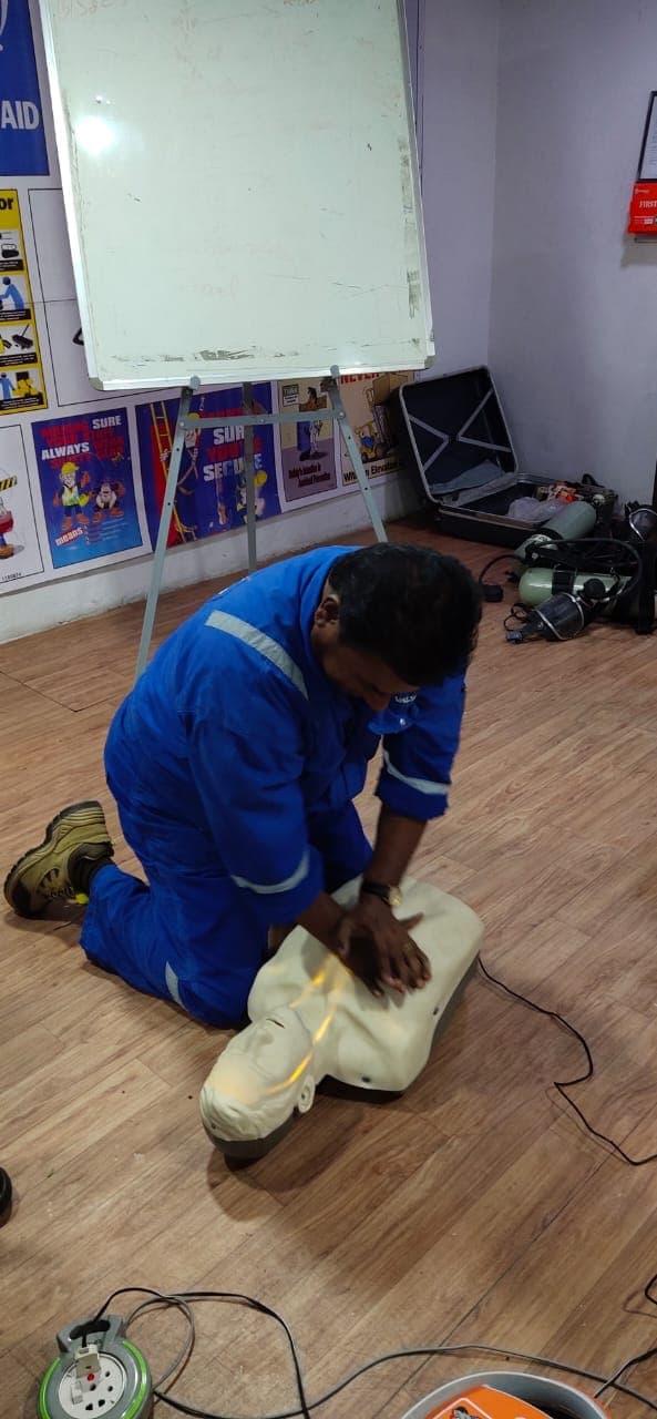 Participant in blue coveralls performing chest compressions on a CPR manikin during training