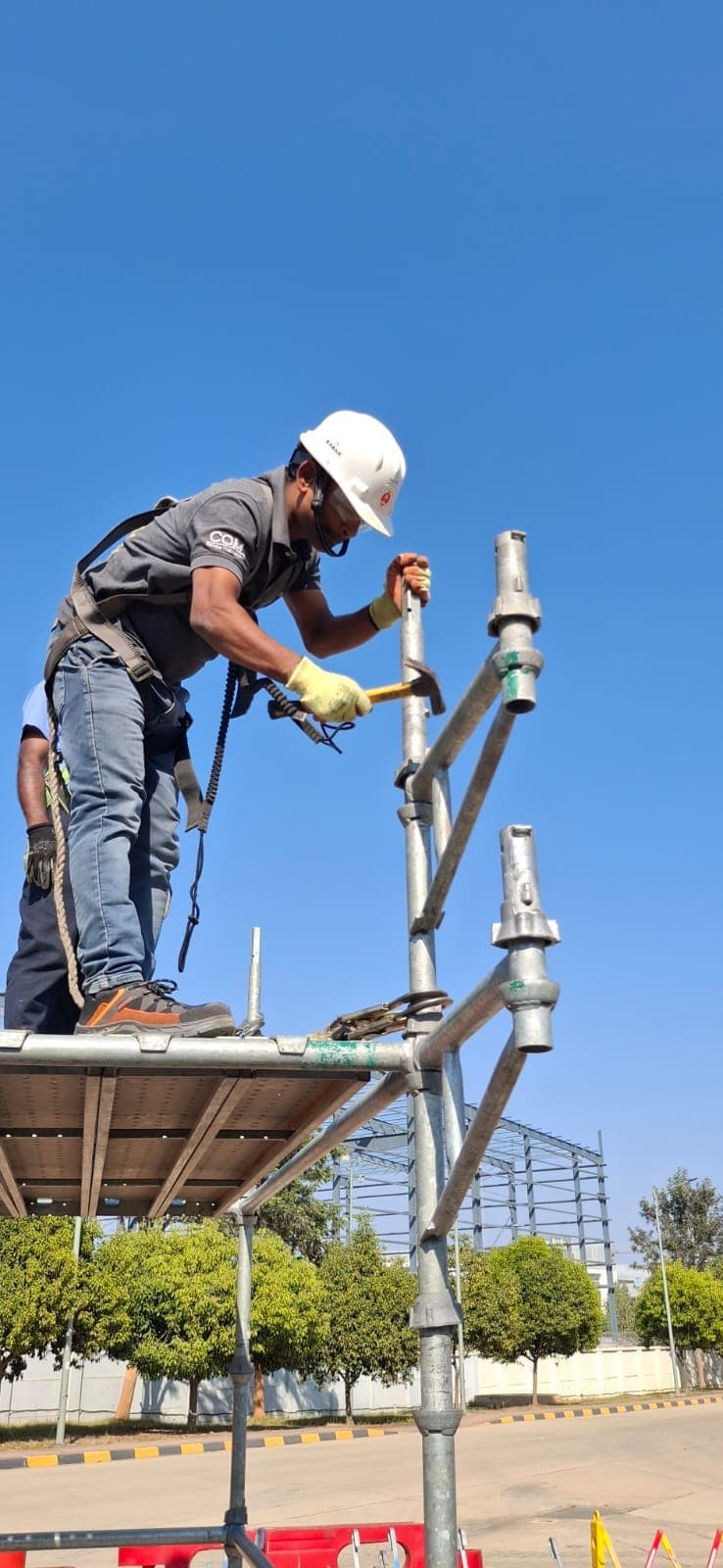 Participant fixing a ladder access bracket to a scaffold against a clear sky