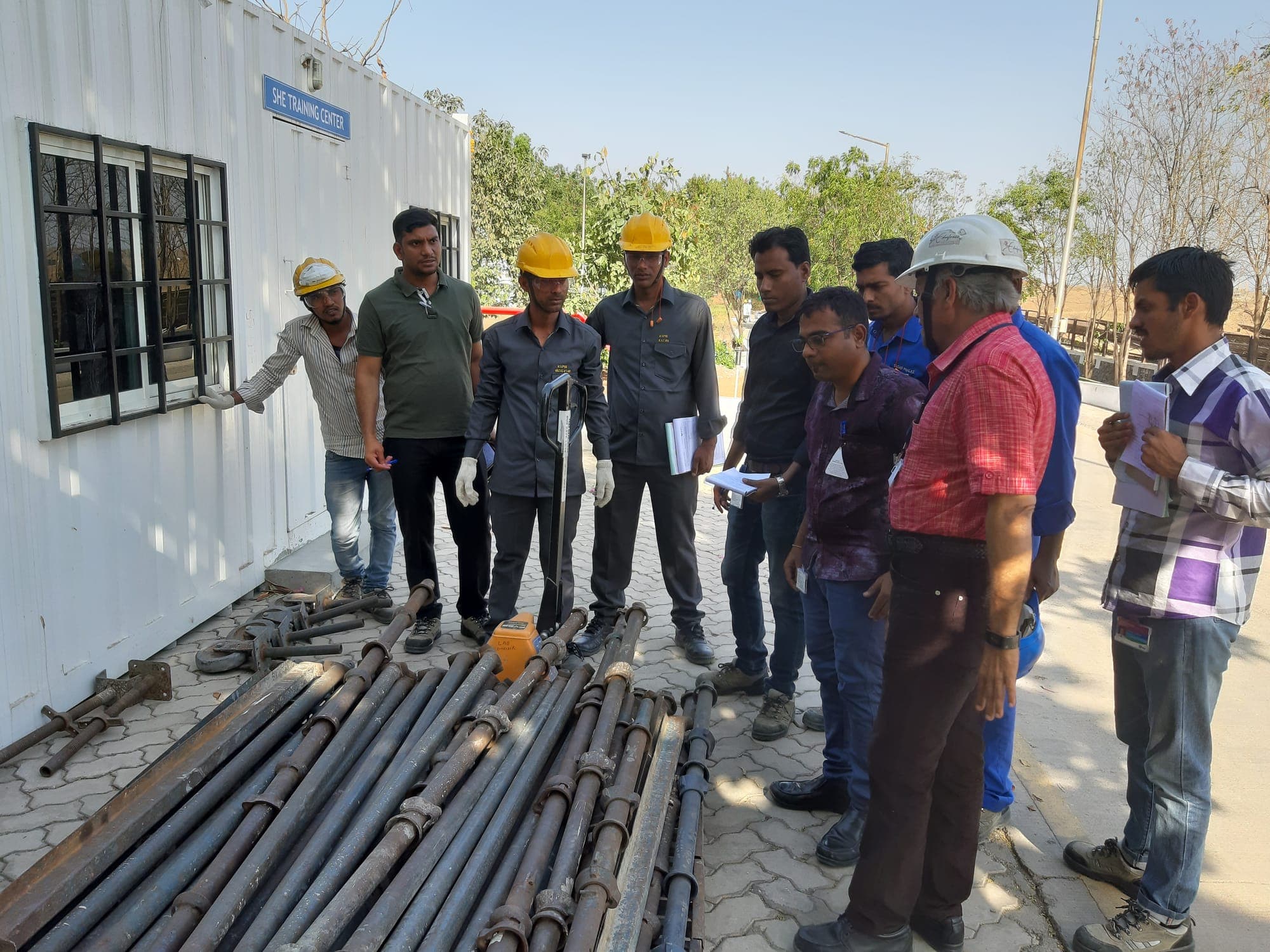 Participants gathered around scaffold standards, ledgers and fittings laid out on the ground while a trainer talks through the components
