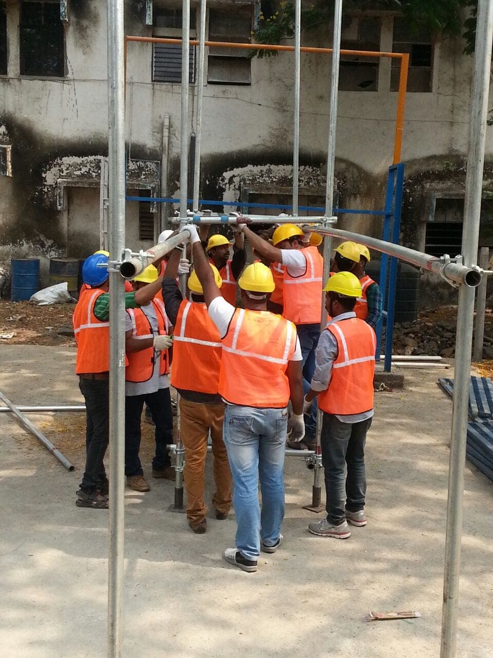 Team in high visibility vests and hard hats erecting a tube and coupler scaffold during training