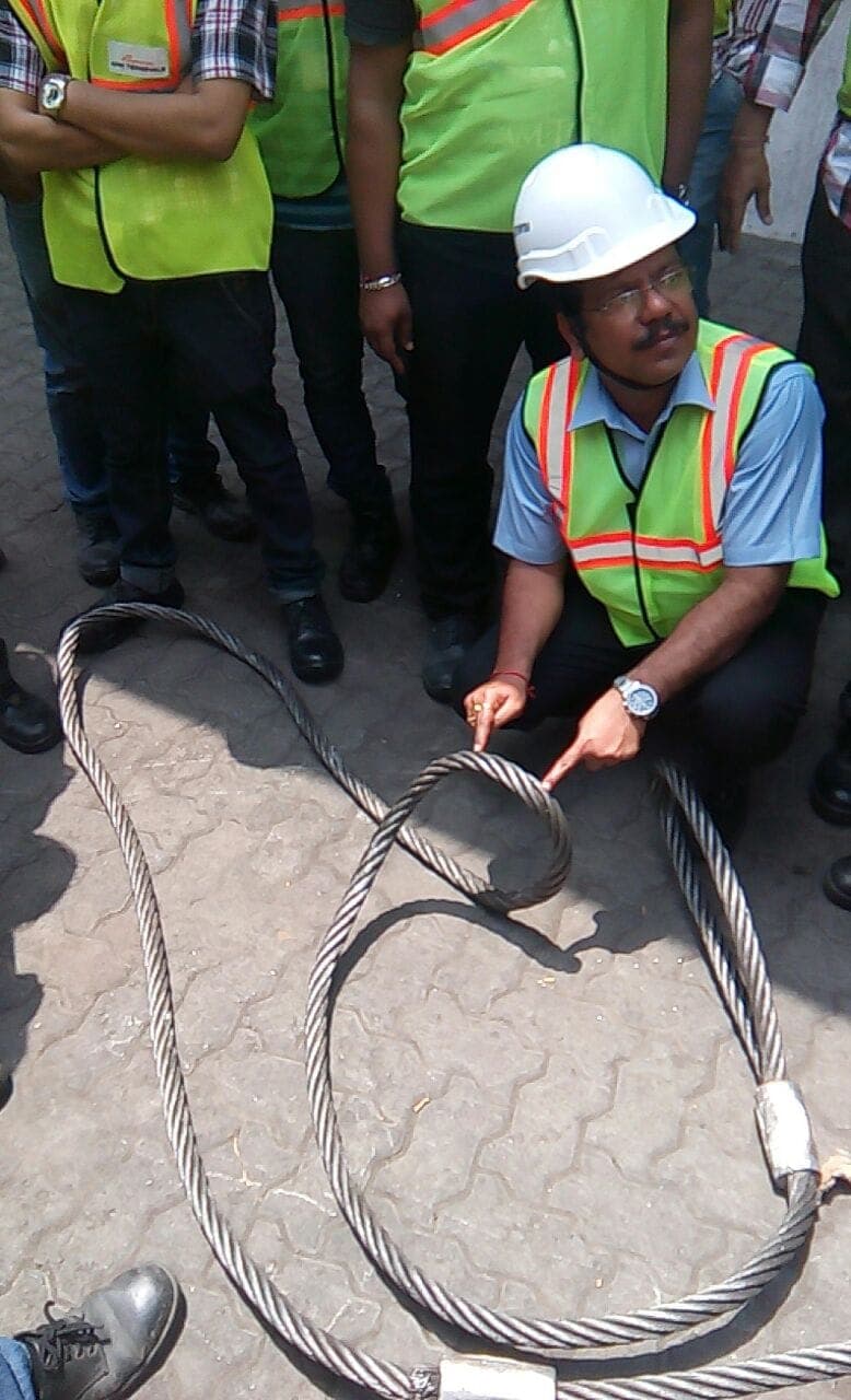Participant in a high-visibility vest inspecting a wire rope sling during rigging training