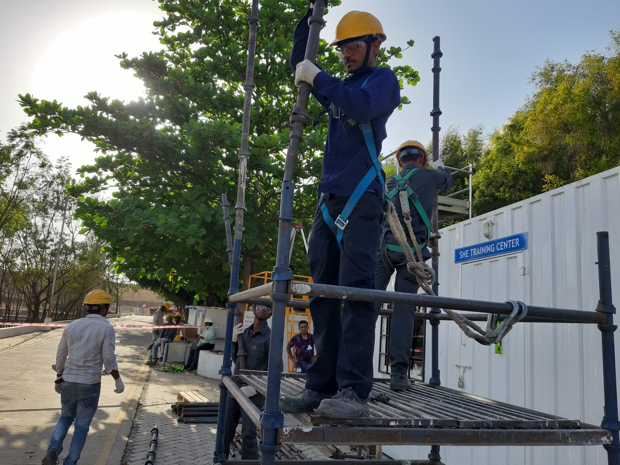 Two participants wearing full-body harnesses, hard hats and safety glasses standing on the boarded platform of a scaffold while fitting a vertical standard