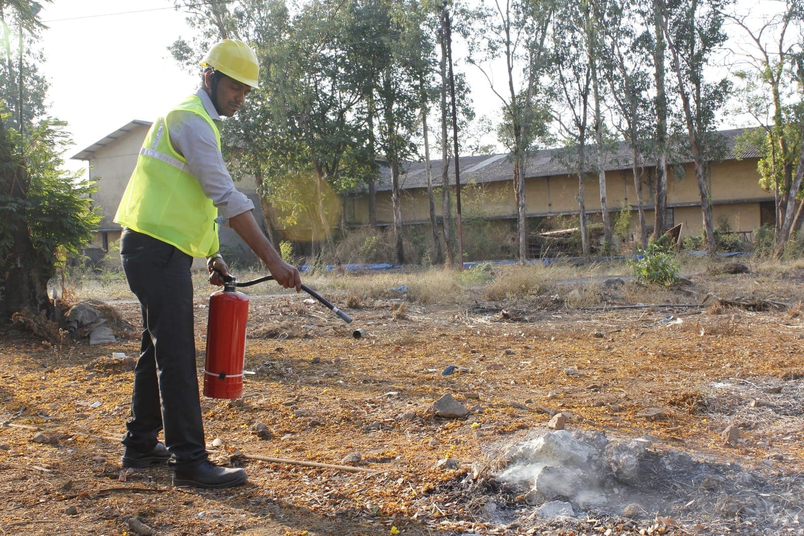 A trainee using a fire extinguisher on a live fire under instructor supervision during a fire safety session