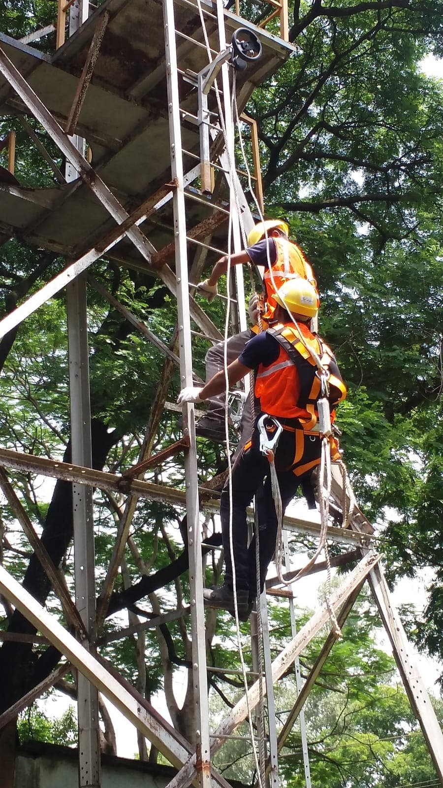 Two climbers in harnesses and helmets ascending a lattice tower