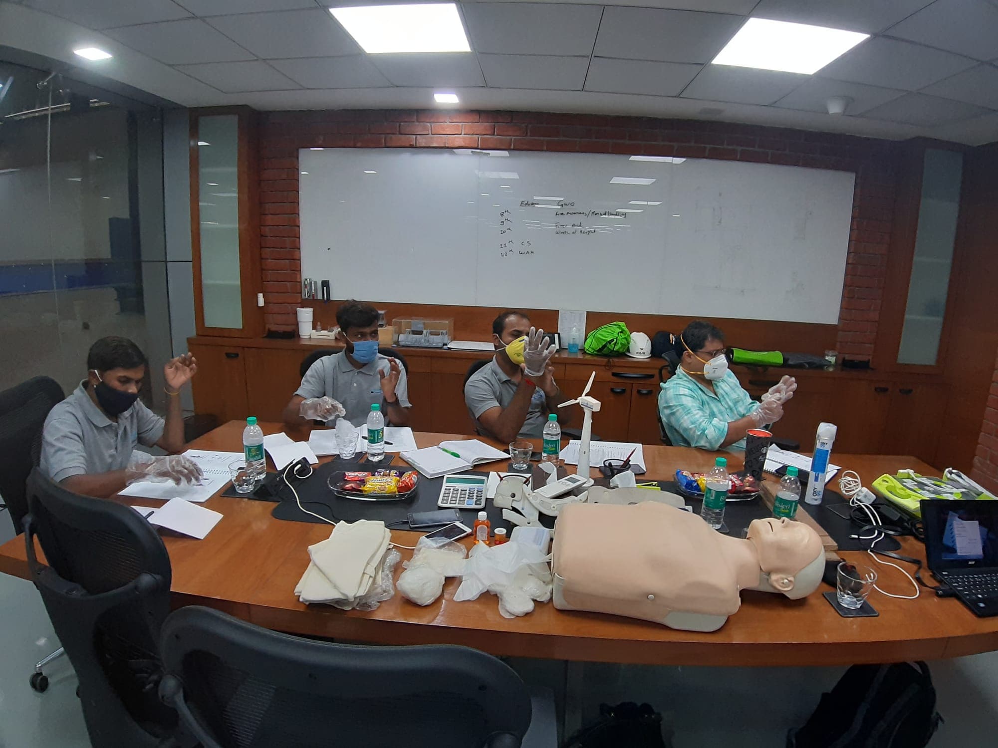Participants seated around a table practising glove technique during a GWO classroom session, with a CPR manikin and a model wind turbine on the table