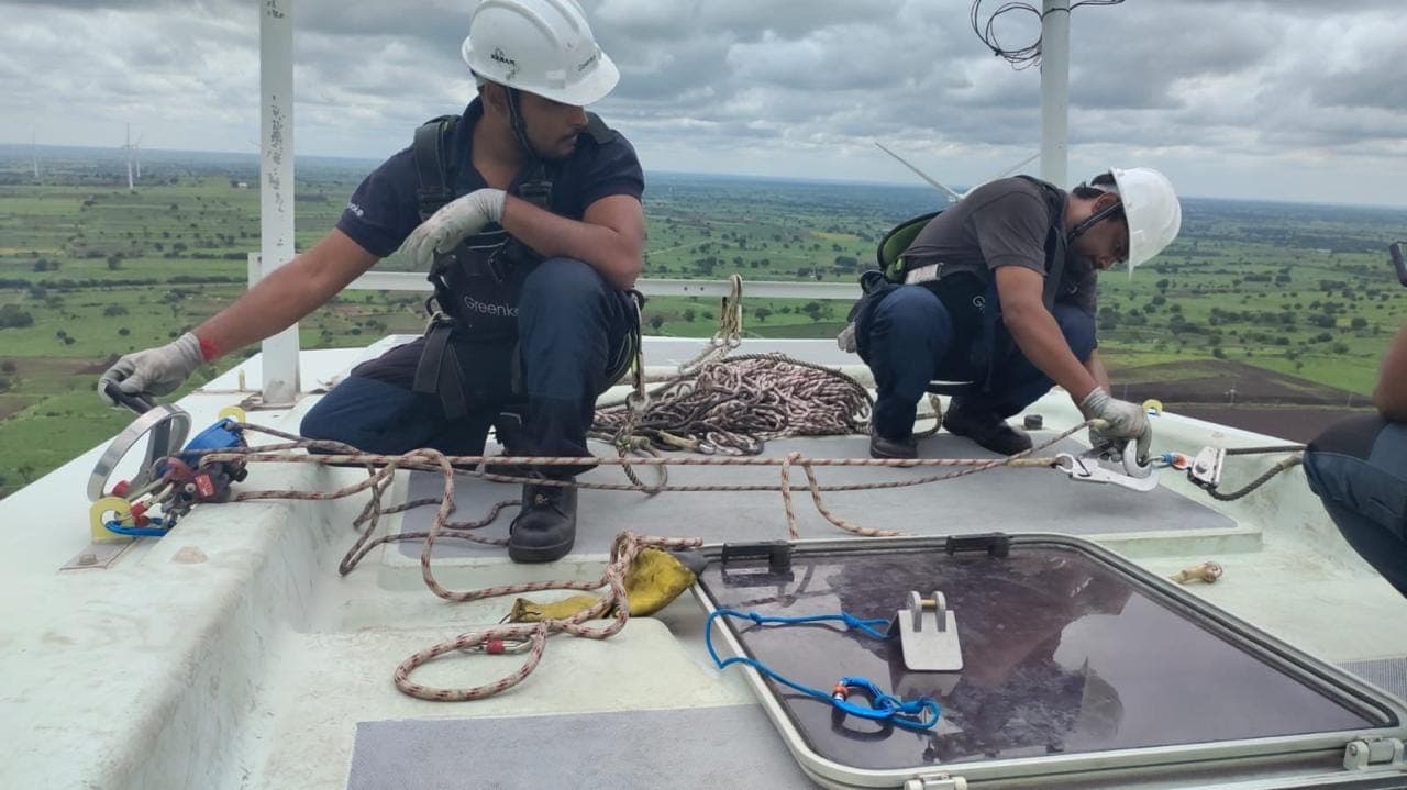 Technicians setting up rescue rigging on a wind turbine nacelle roof above open countryside