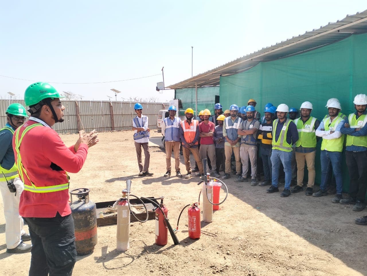 Trainer briefing site workers in helmets beside fire extinguishers at an open site